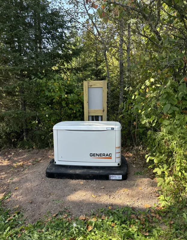 Portable generator on a black base in a wooded outdoor area, with a wooden-framed sign behind it.