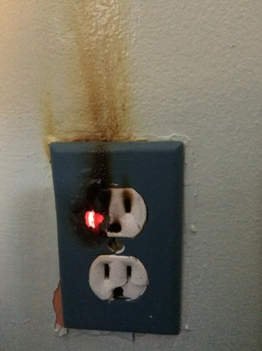 Burned electrical outlet with scorch marks and a glowing red light on the upper socket.