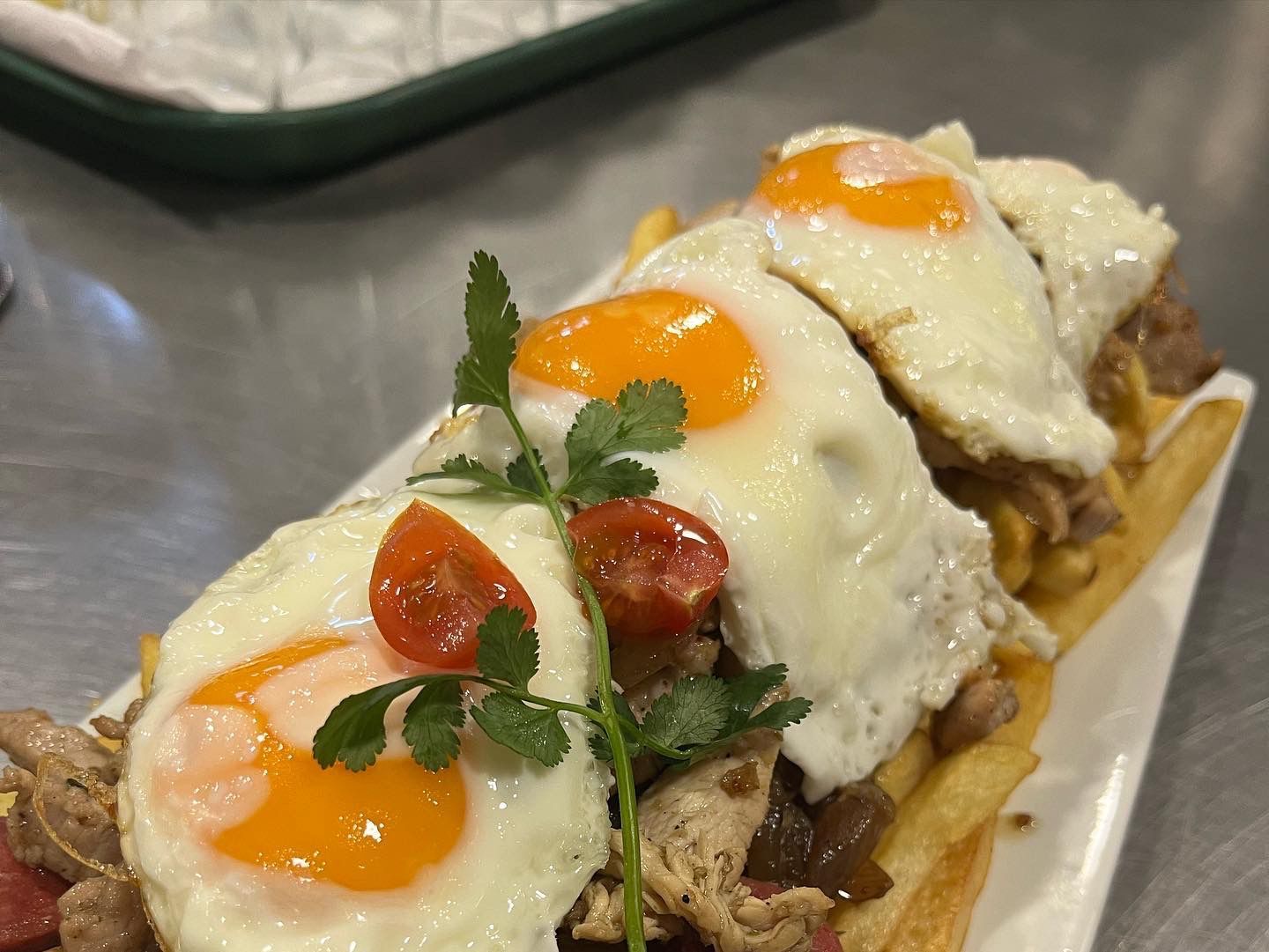 Huevos fritos sobre una baguette cubiertos con carne, papas fritas, tomates y hierbas.
