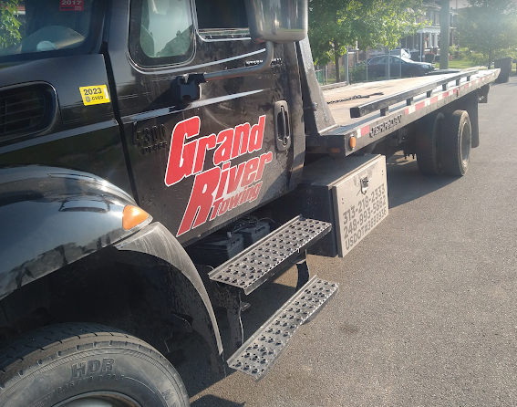 Black flatbed tow truck with red “Grand Auto” logo parked along a street