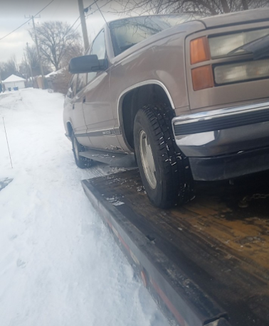 Tan pickup truck parked on a snowy roadside, viewed from the front side.