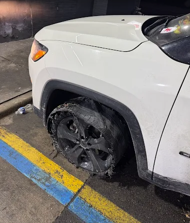 White SUV with a damaged front-left tire parked by a curb with blue and yellow lines.