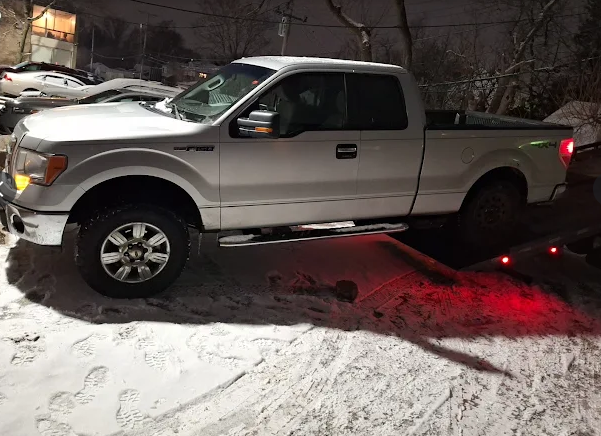 Silver pickup truck stuck on snowy road at night, with red taillights glowing.