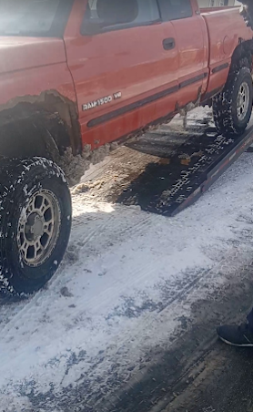 Red pickup truck parked on a snowy road, with a wet patch beside it.