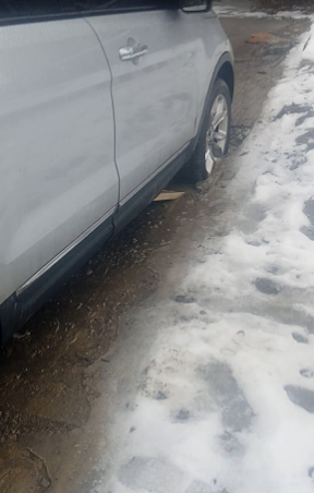Silver car parked beside a snowy, slushy curb on a wet street