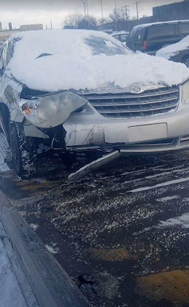 Snow-covered damaged silver SUV with a crumpled front end on a wet roadside in winter