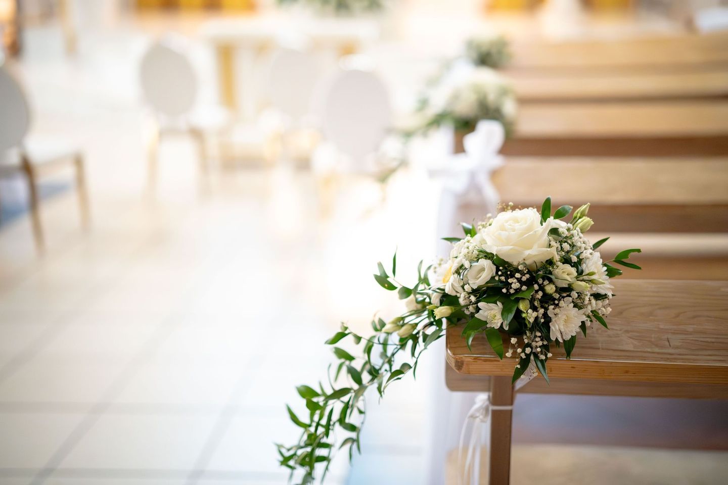 White floral bouquet with greenery bench boutquets, church pew in a bright ceremony venue
