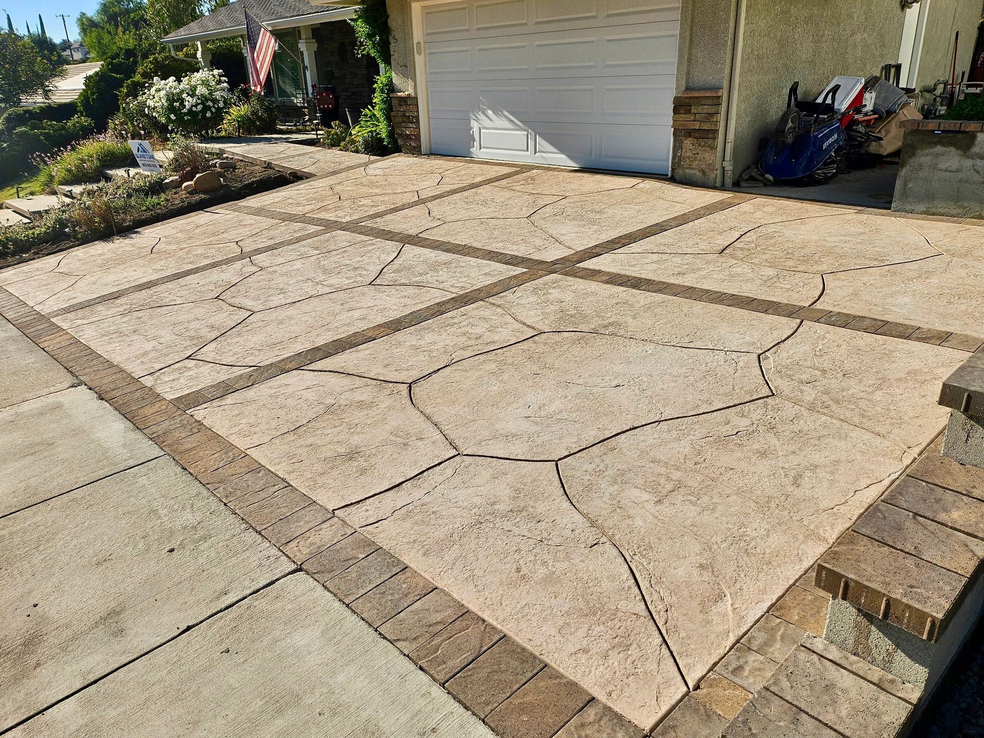Cracked concrete driveway in front of a white garage, with brick border and a blue scooter at right.