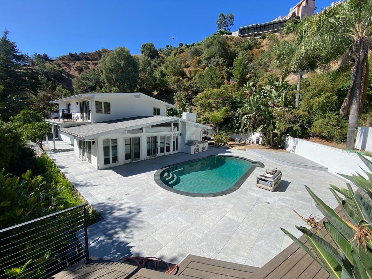 White hillside villa with a curved swimming pool and stone terrace surrounded by lush greenery