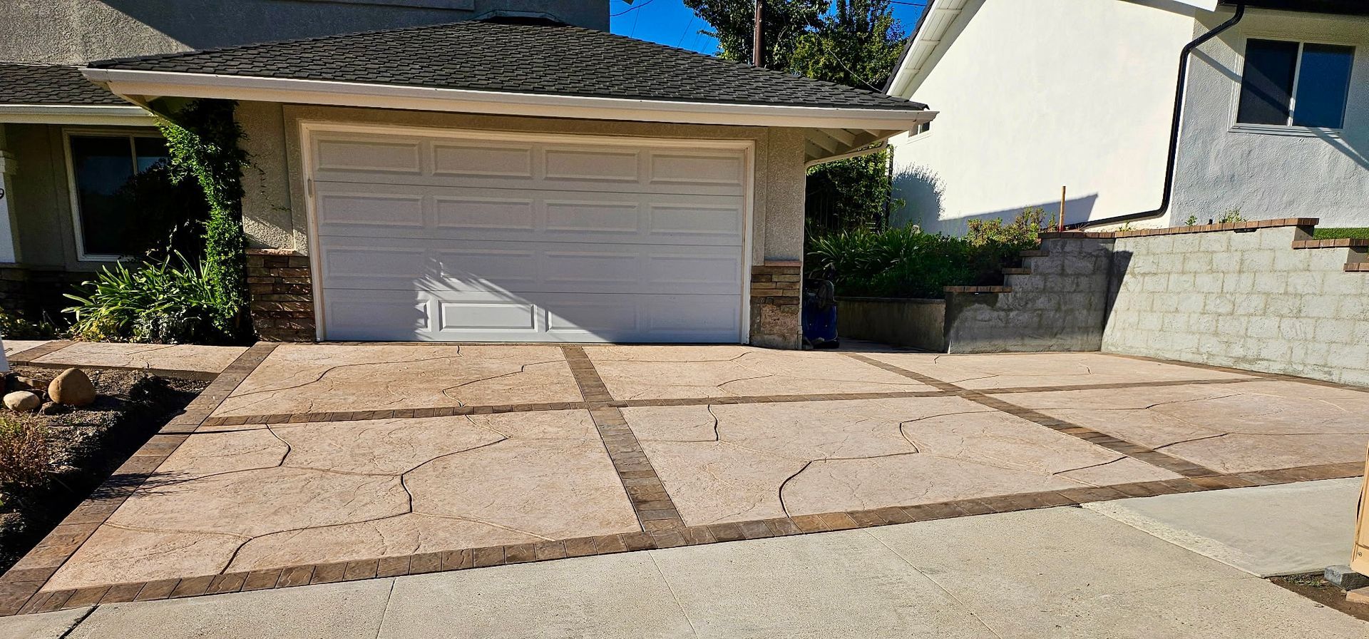 Suburban house front with a white garage door and concrete driveway under bright sunlight
