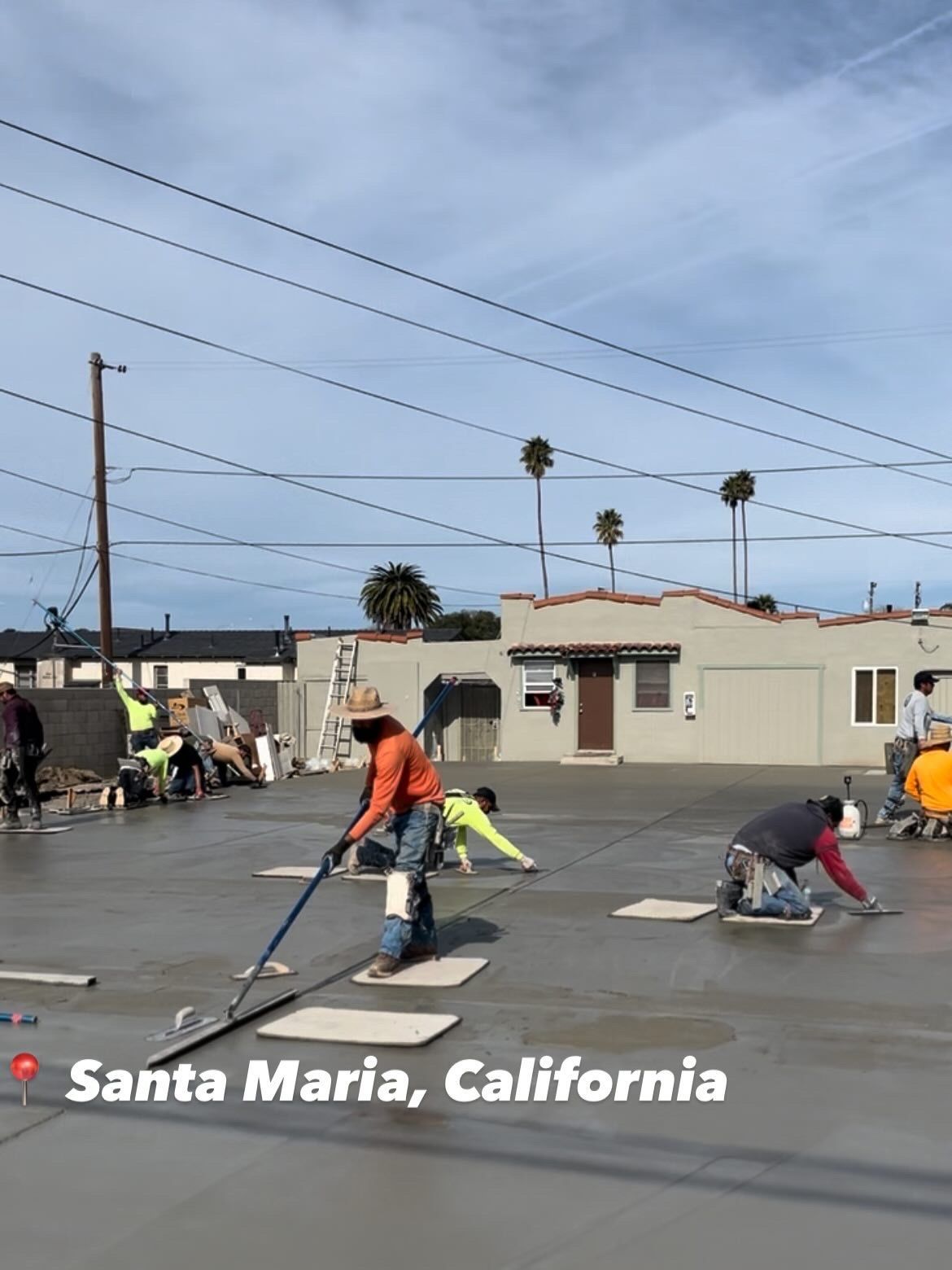 Workers sanding pavement in a parking lot near low buildings, Santa Maria, California.