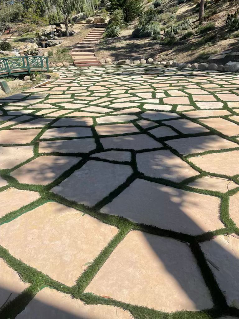 Stone garden path with irregular tan pavers and green grass joints leading uphill through trees