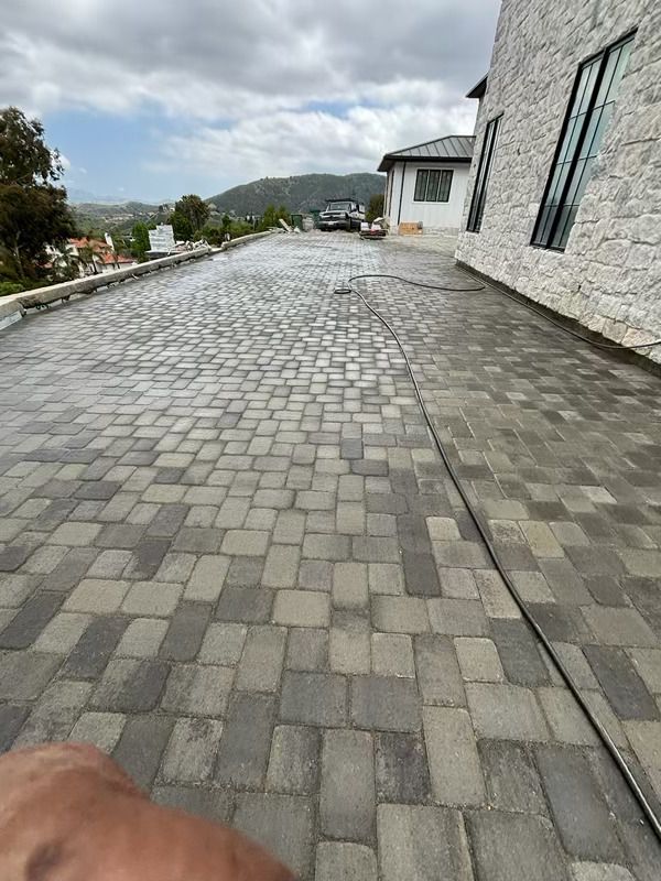 Stone-paved driveway beside a modern house, leading toward hills under a cloudy sky.