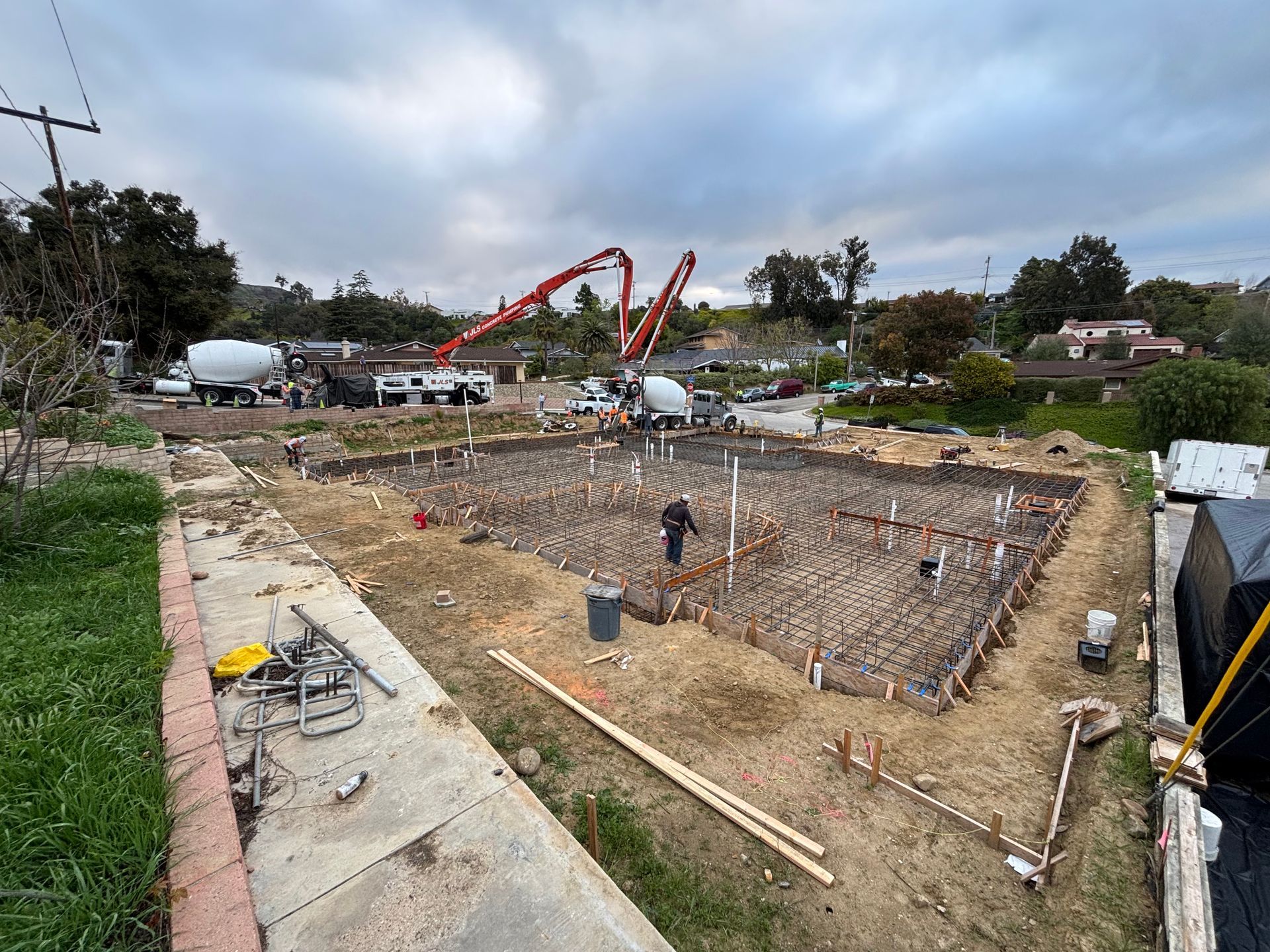Construction site with a large excavated foundation, rebar, and a concrete truck in the background