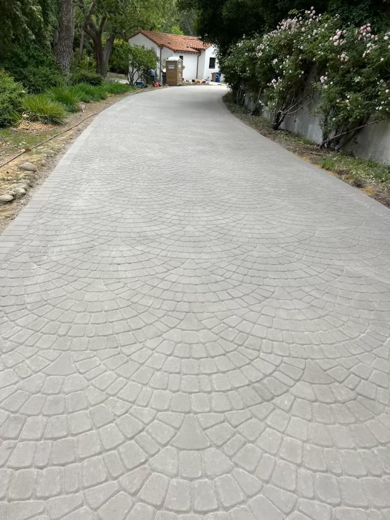 Curved cobblestone driveway leading to a white house, lined with greenery and stone walls