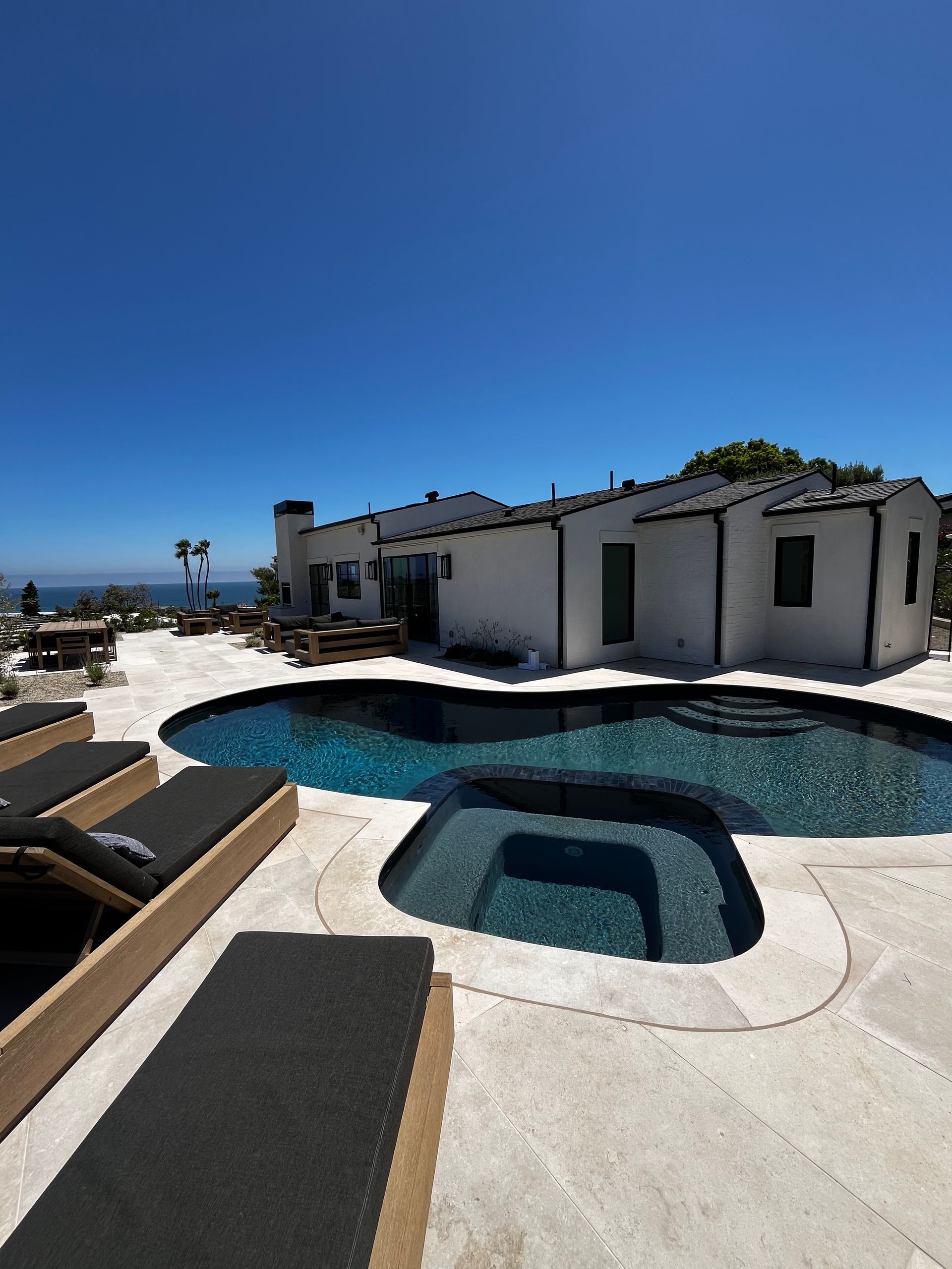 Modern pool patio beside a white house under a clear blue sky