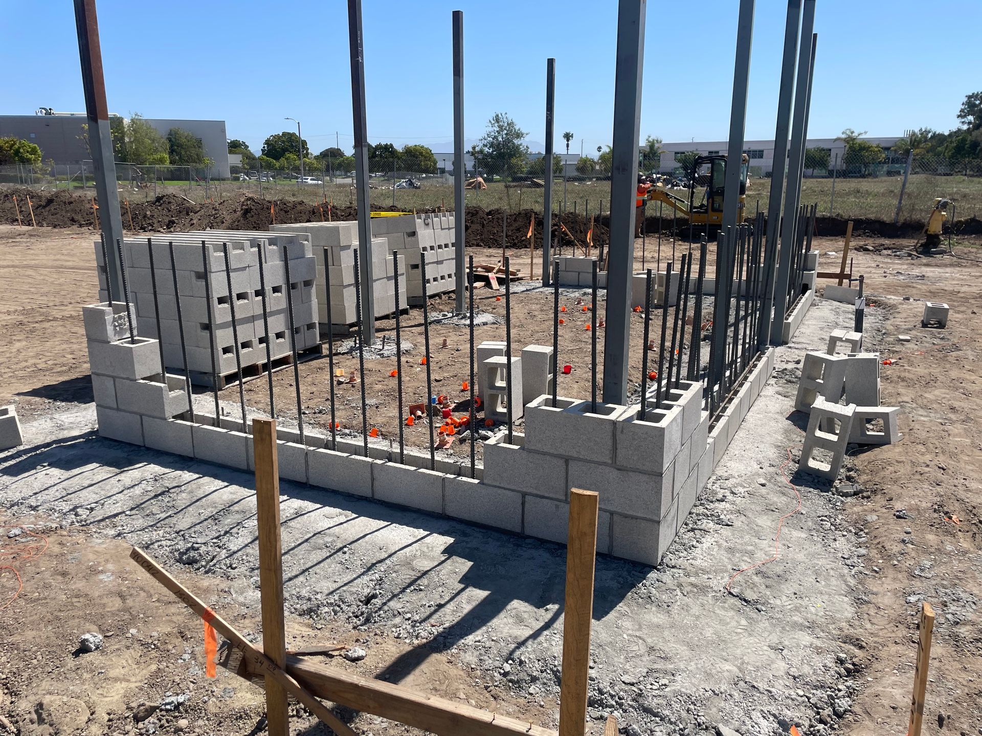 Partially built concrete block foundation with vertical rebar on a construction site under clear skies