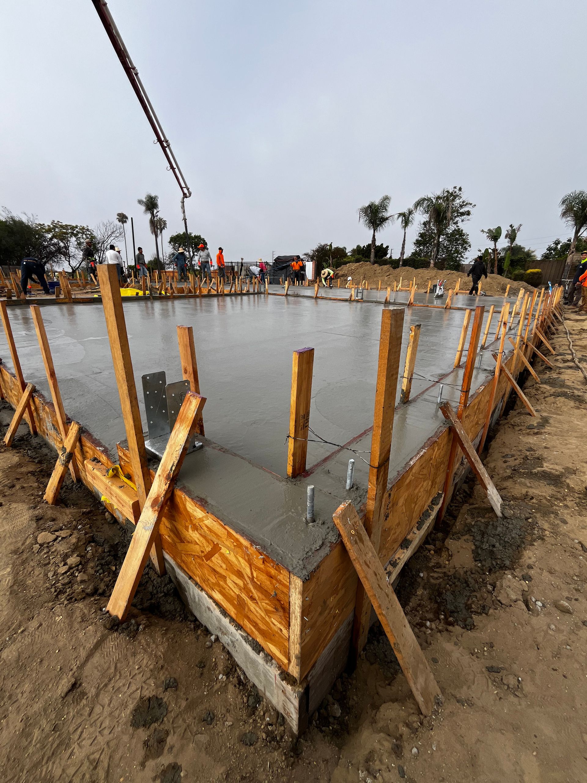 Fresh concrete slab foundation with wooden formwork and rebar stakes on a construction site.