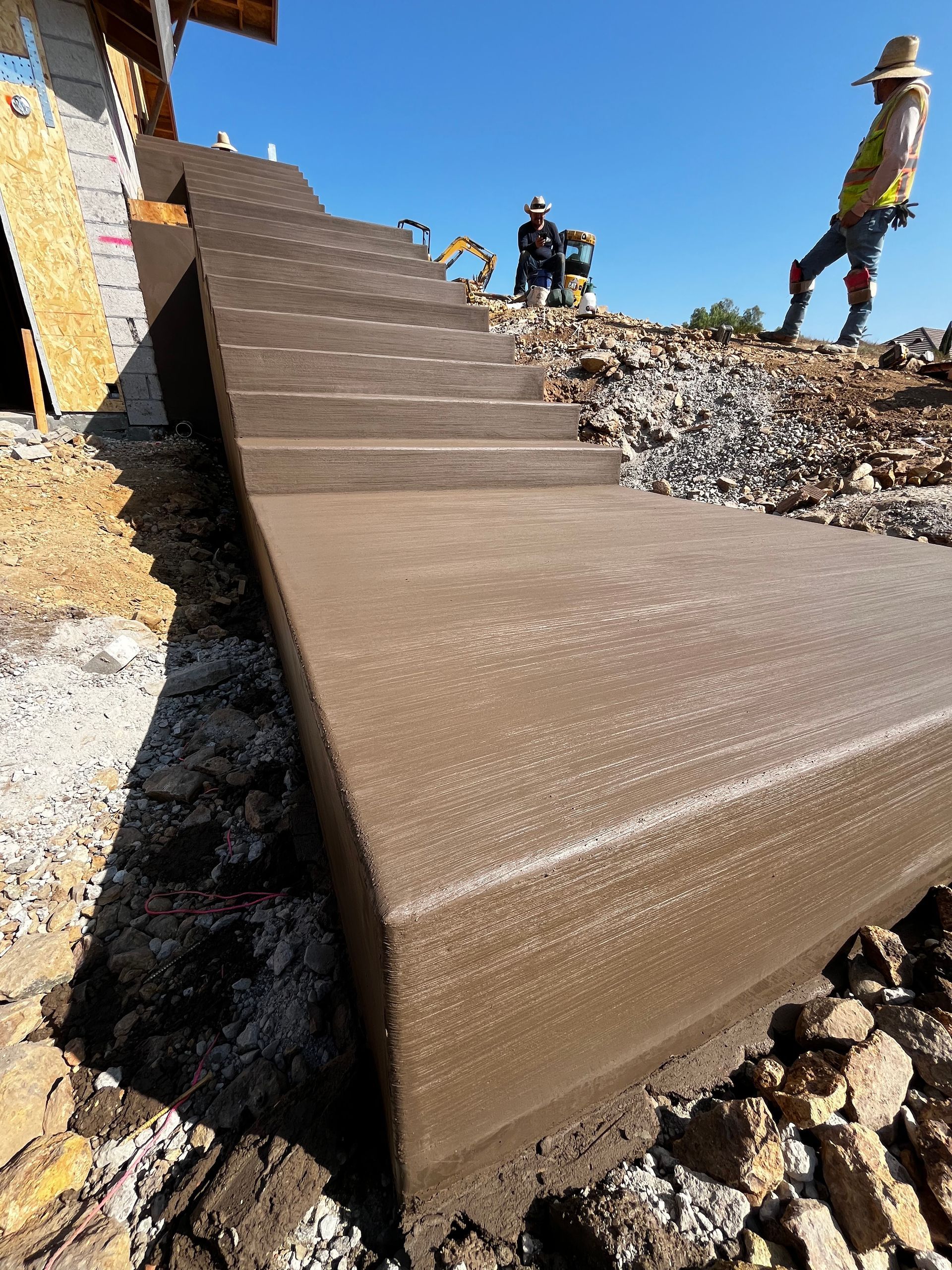 Fresh concrete stairway being built at a construction site, with workers nearby and gravel around it