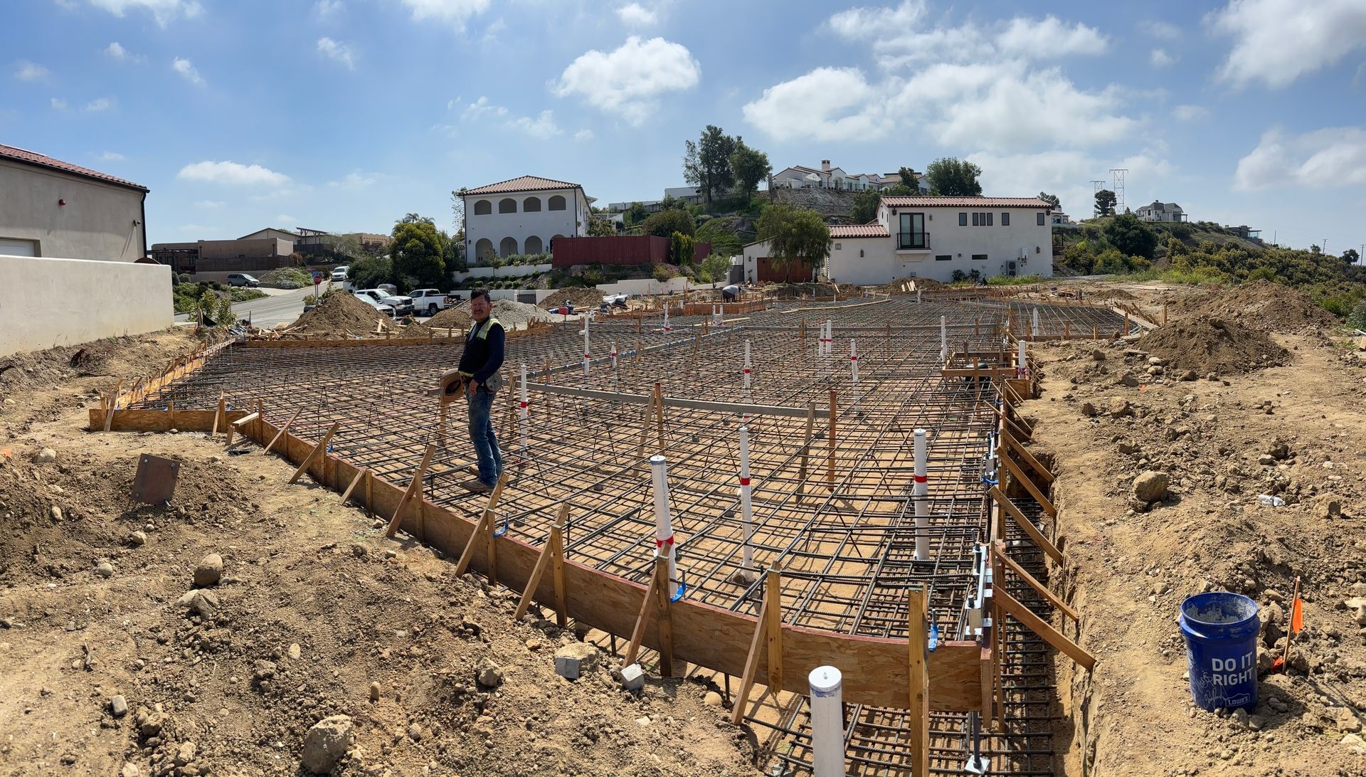 Construction site with rebar foundation grid and a worker standing on the footing area under a sunny sky