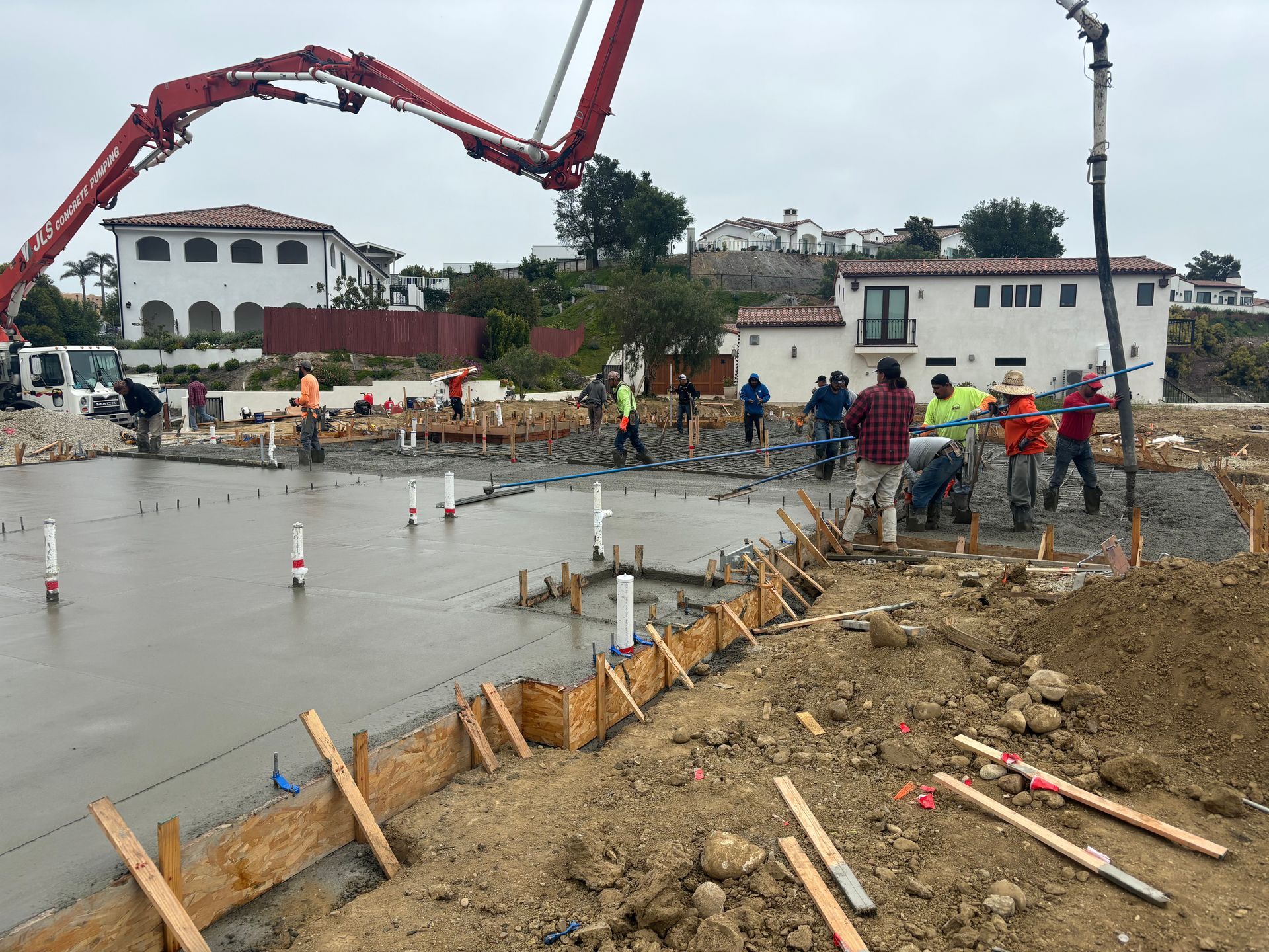 Construction workers pouring concrete on a roadside site beside a flooded area and a red pump truck