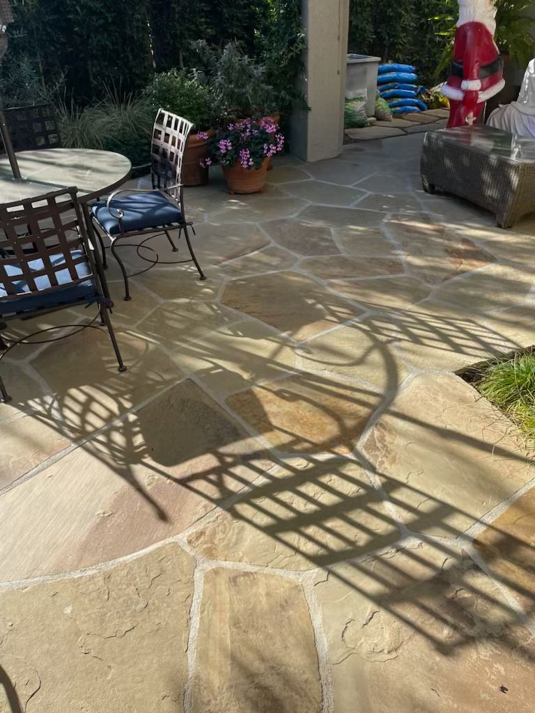 Sunlit stone patio with metal chairs, table, potted plants, and long shadow patterns