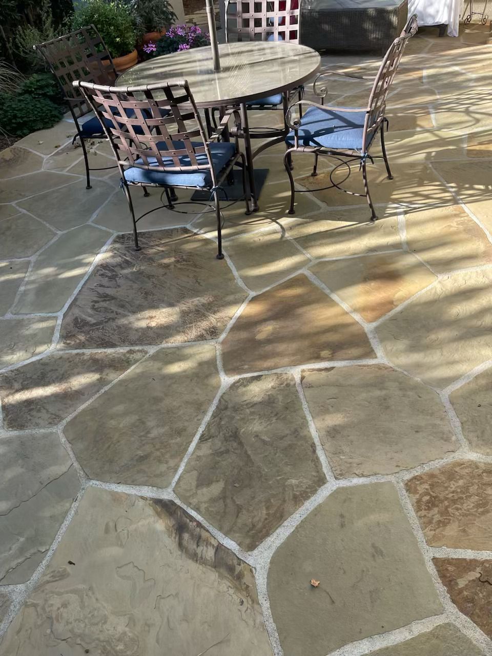 Stone patio with round outdoor table and four metal chairs in sunlight
