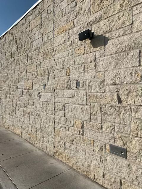 Stone block wall beside a sidewalk, with a black wall-mounted light and metal fixtures.