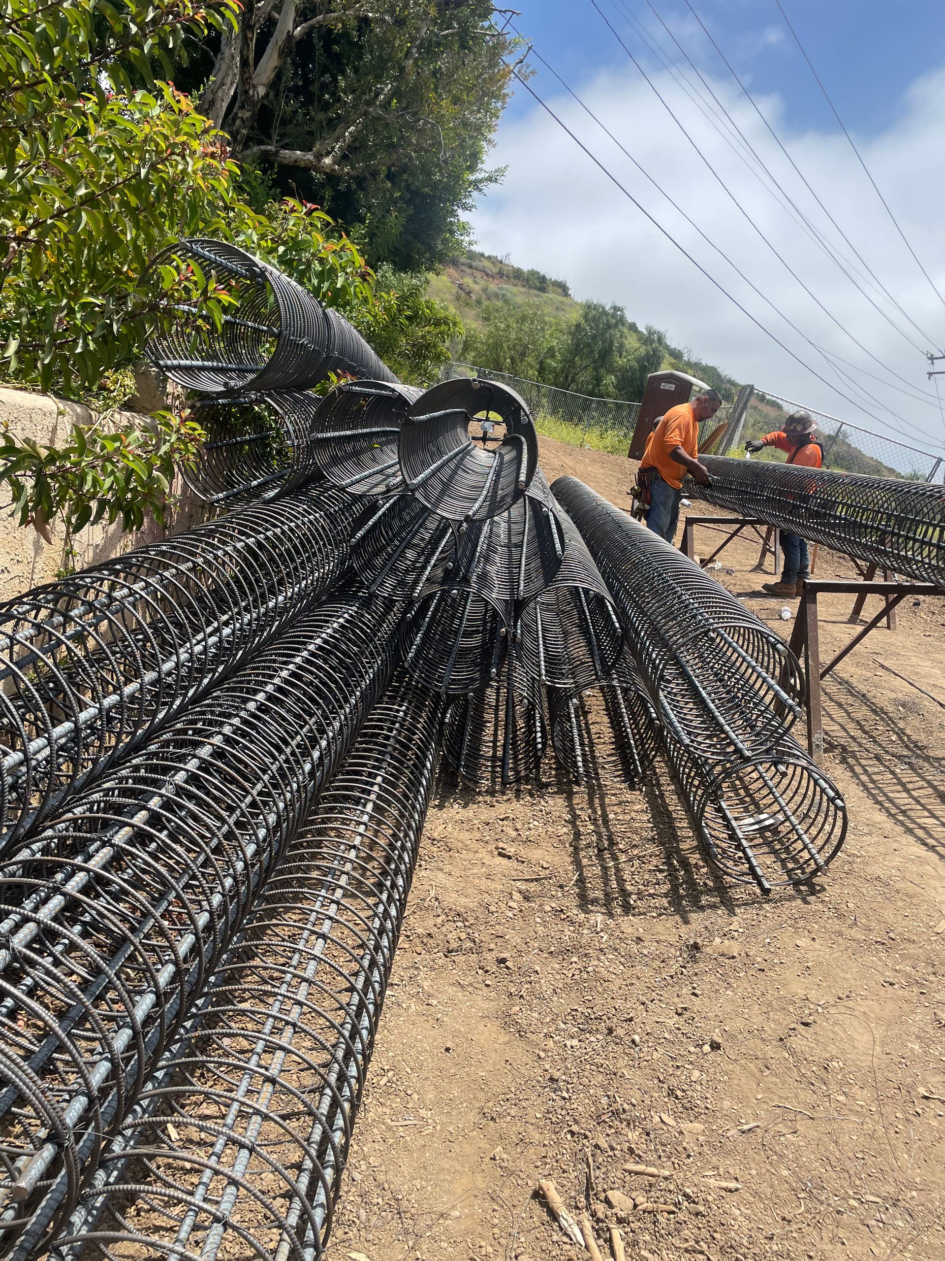 Bent rebar bundles at a roadside construction site with workers in orange vests in the background