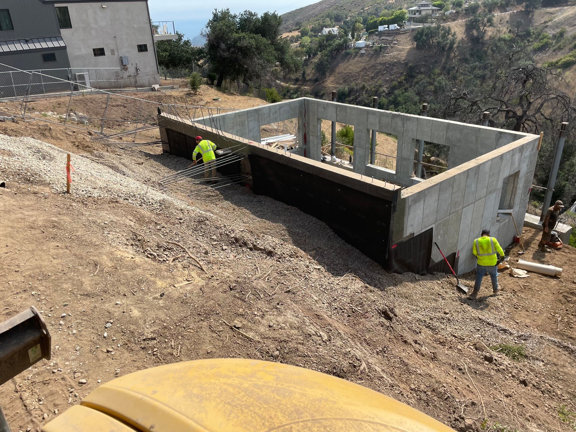 Construction site with concrete foundation walls on a dirt slope and two workers in neon safety gear