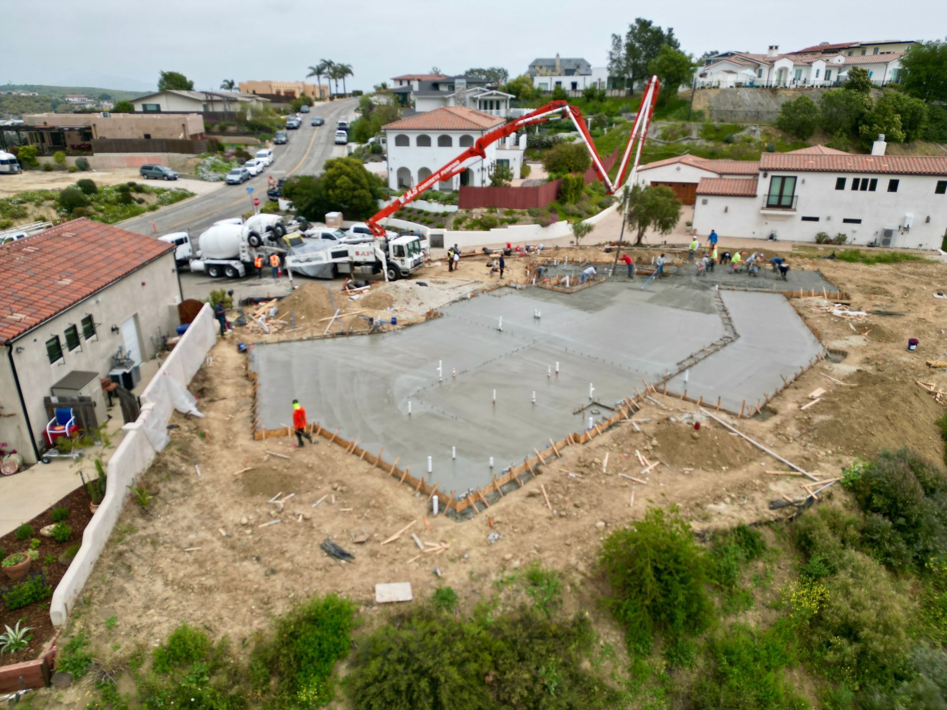 Construction site with a large concrete foundation slab and workers in a residential neighborhood.
