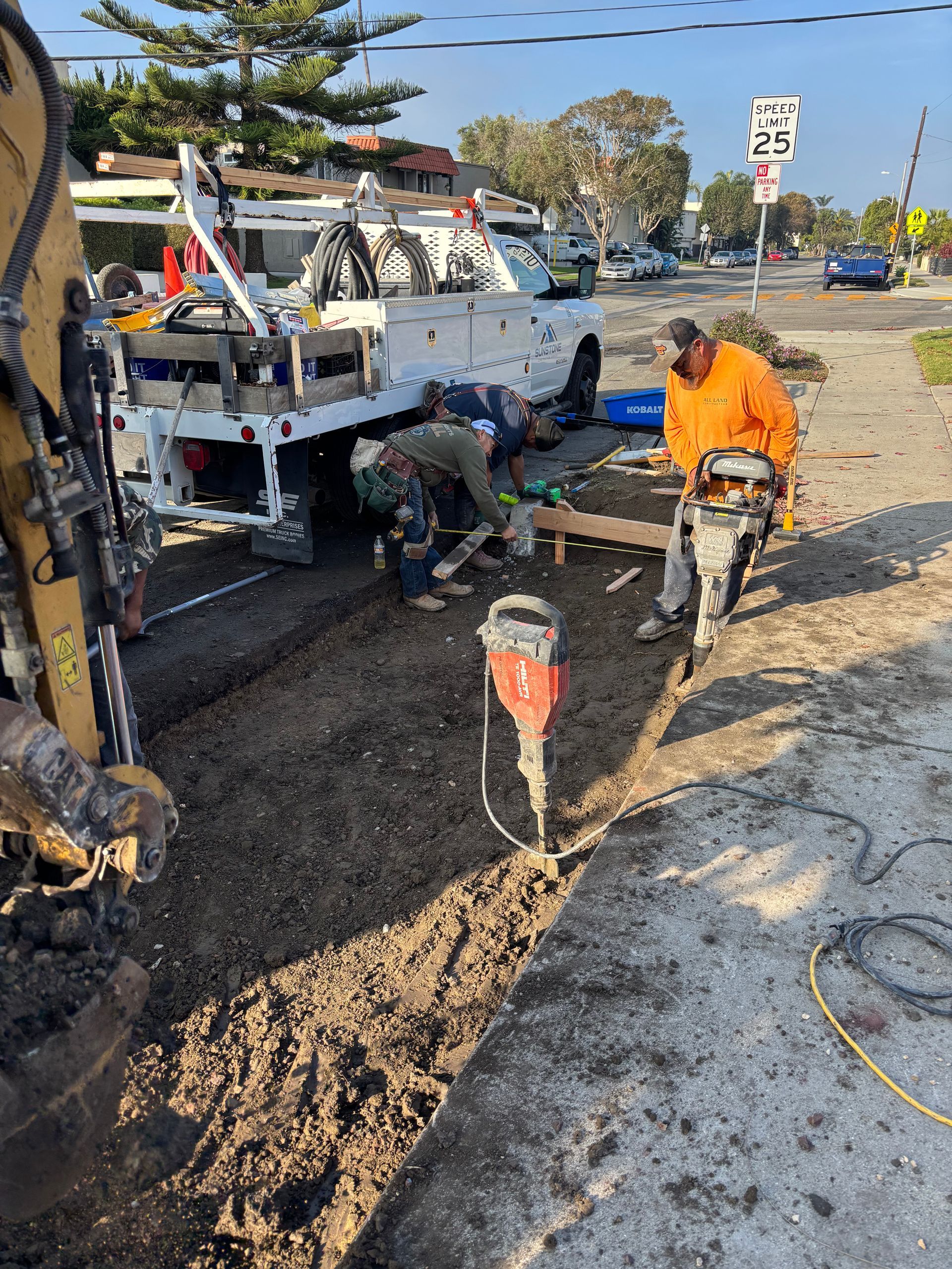 Roadwork crew repairing a trench beside a white utility truck on a sunny street