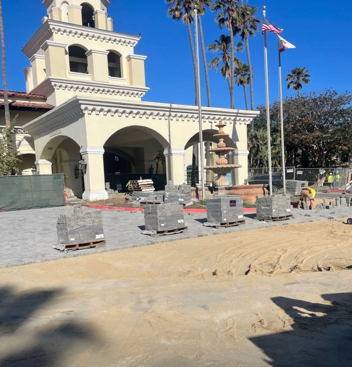 Historic building entrance with arches, flags, and stacked construction materials in front under a sunny sky