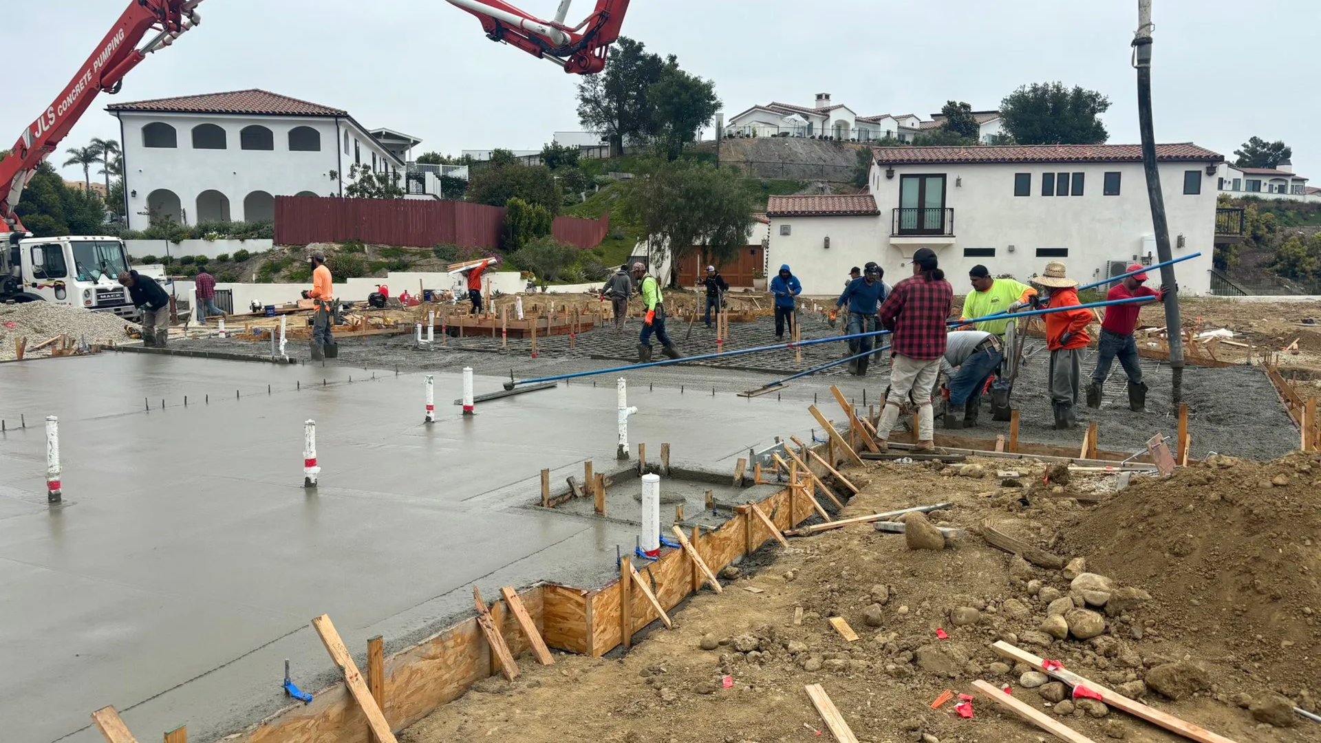 A construction crew pours concrete for a building foundation with a boom pump truck on a sunny day.