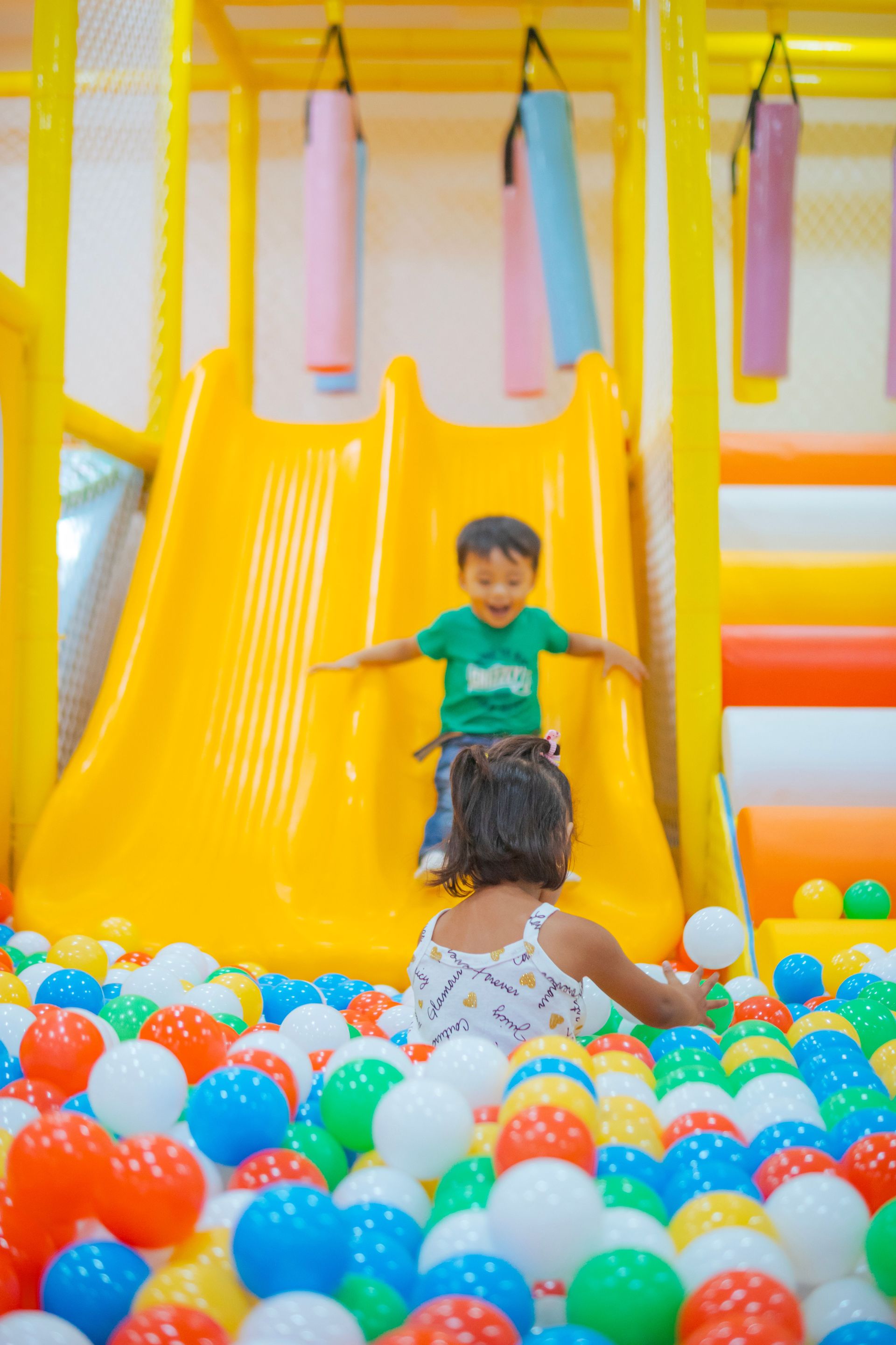 Children playing in a colorful ball pit at the base of a bright yellow slide