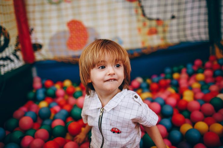 Child sitting in a colorful ball pit, wearing a white shirt and looking to the side