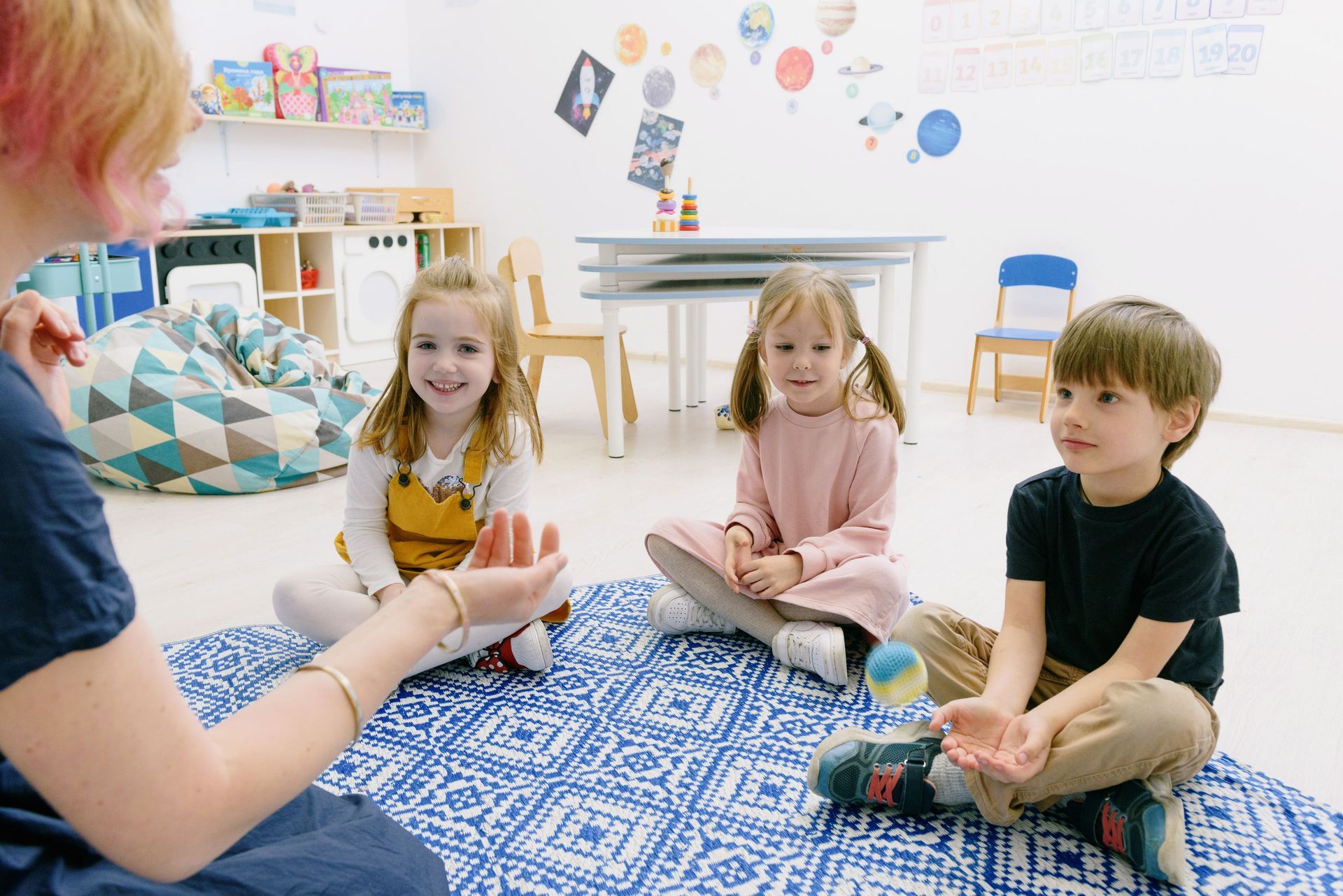 Children sitting in a circle with a teacher in a bright classroom, listening during a group activity