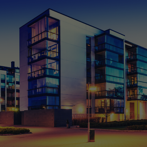 Modern apartment buildings at dusk with glass balconies and warm interior lights
