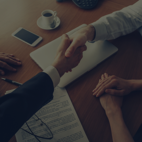 Business handshake over documents at a meeting table with coffee and a smartphone.