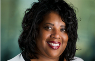 Smiling woman with curly black hair and red lipstick against a blurred green background