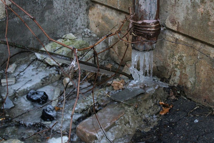 De l'eau glacée ruisselait d'un tuyau de descente rouillé sur un sol jonché de débris.