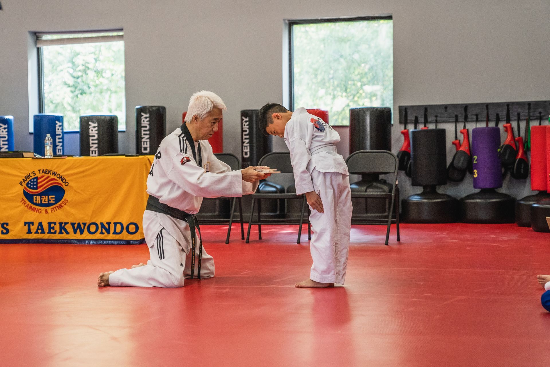 A man is kneeling down next to a young boy on a taekwondo mat.
