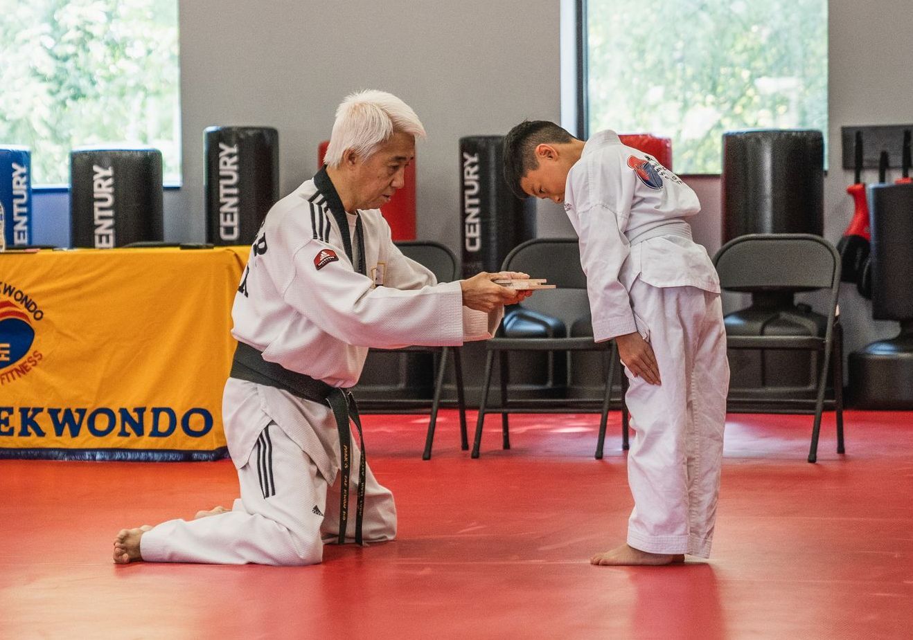 A woman is kneeling down next to a boy in a karate class.