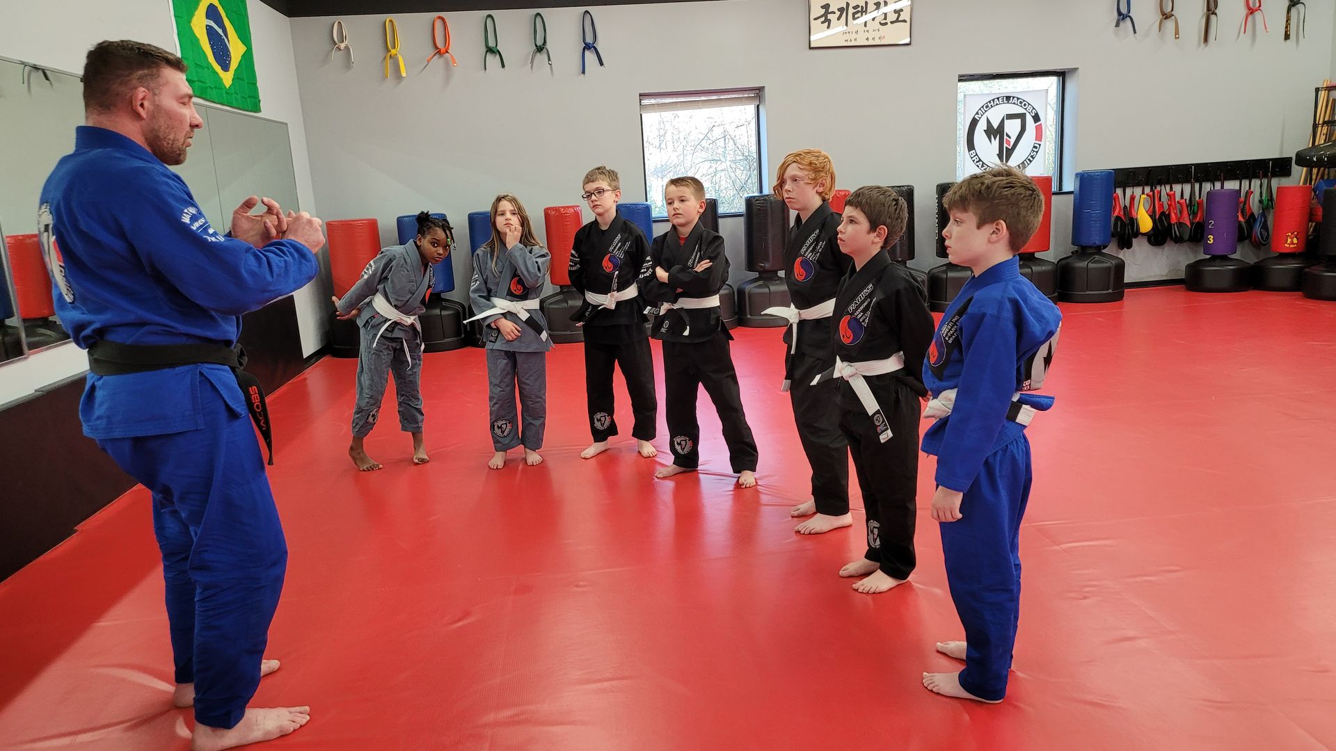 A group of children are standing in a circle in a gym while a man talks to them.