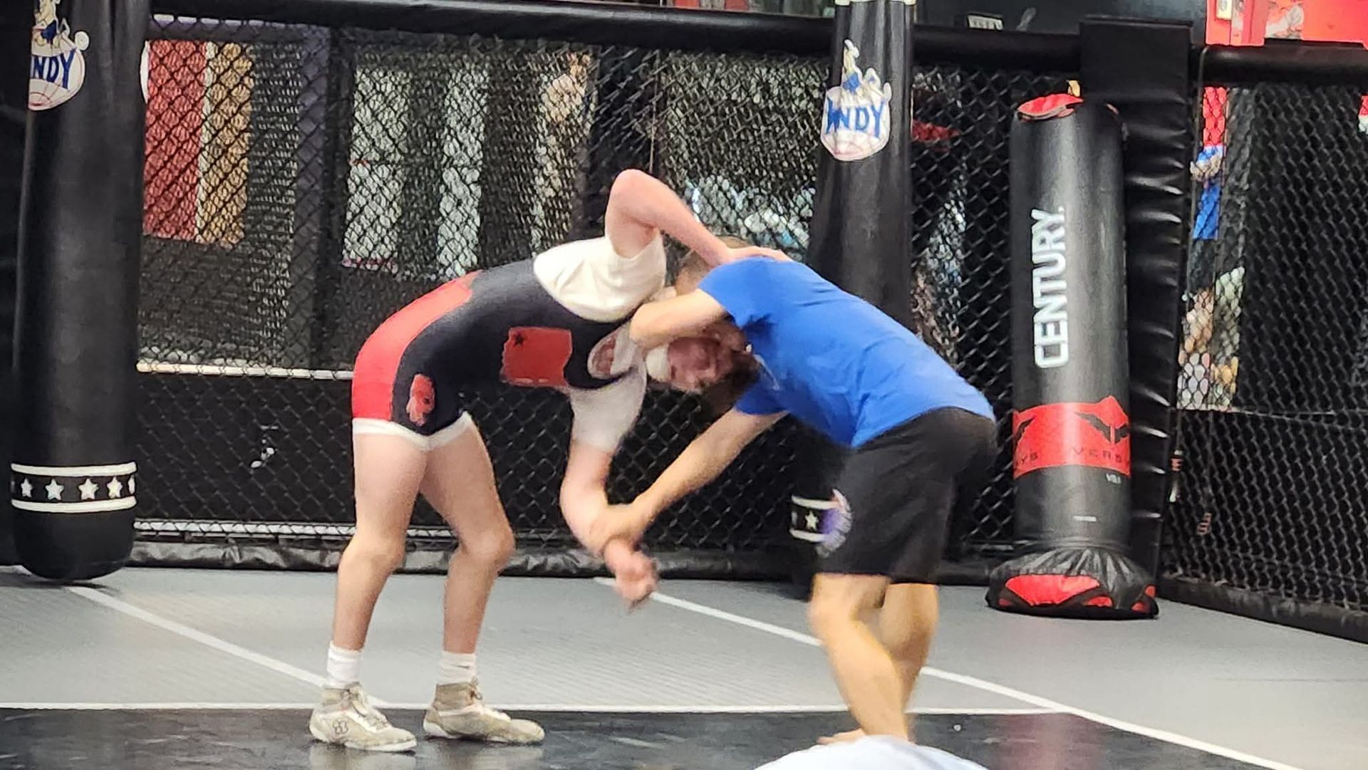 Two men are wrestling on a mat in a gym.