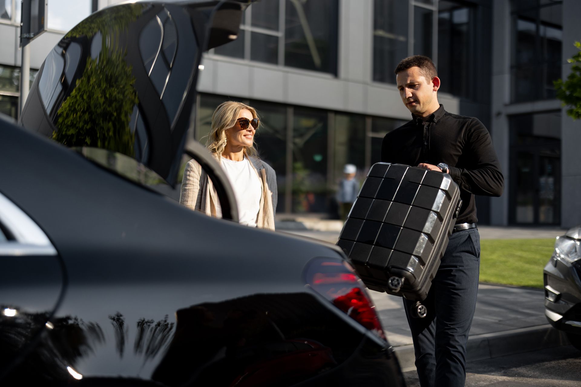 Man loading luggage into black car for woman outside building