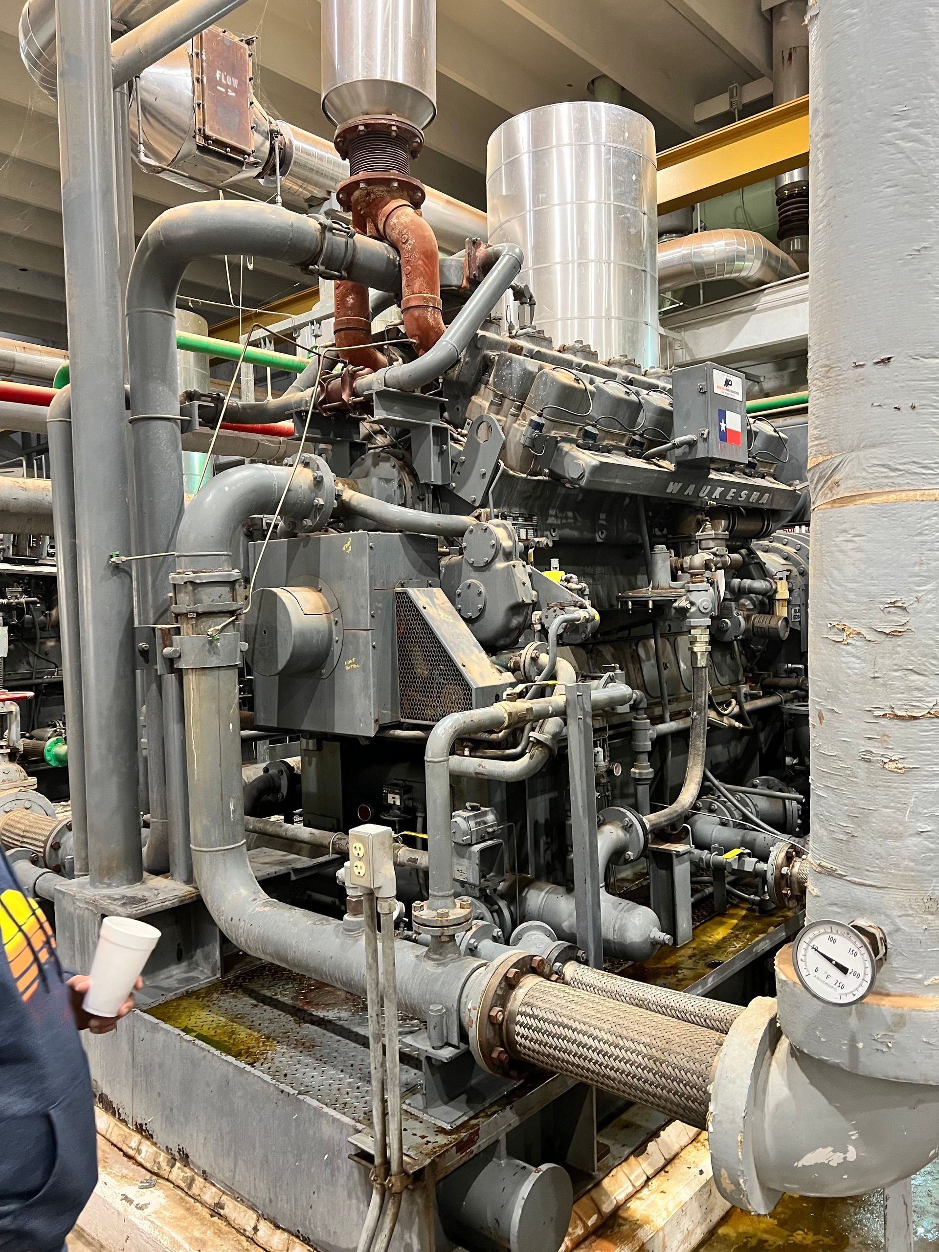 A man is standing next to a large engine in a factory.