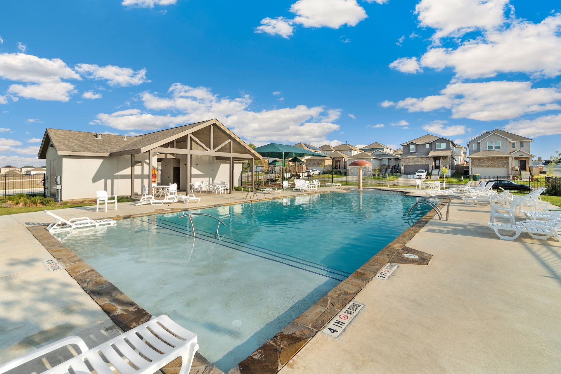 Outdoor resort-style pool with lounge chairs, a cabana, and houses under a blue sky