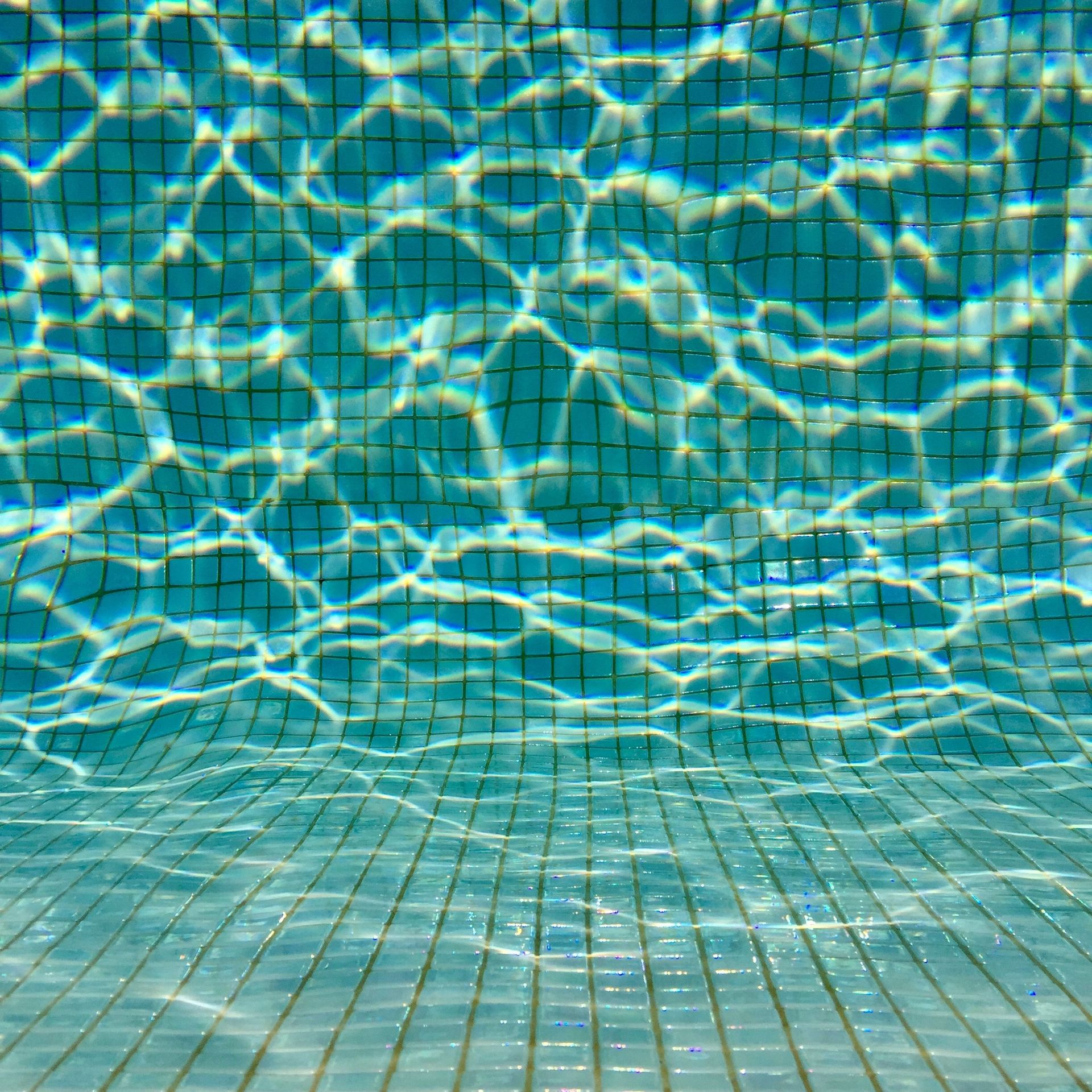 Blue swimming pool water with sunlight reflections and tiled floor beneath
