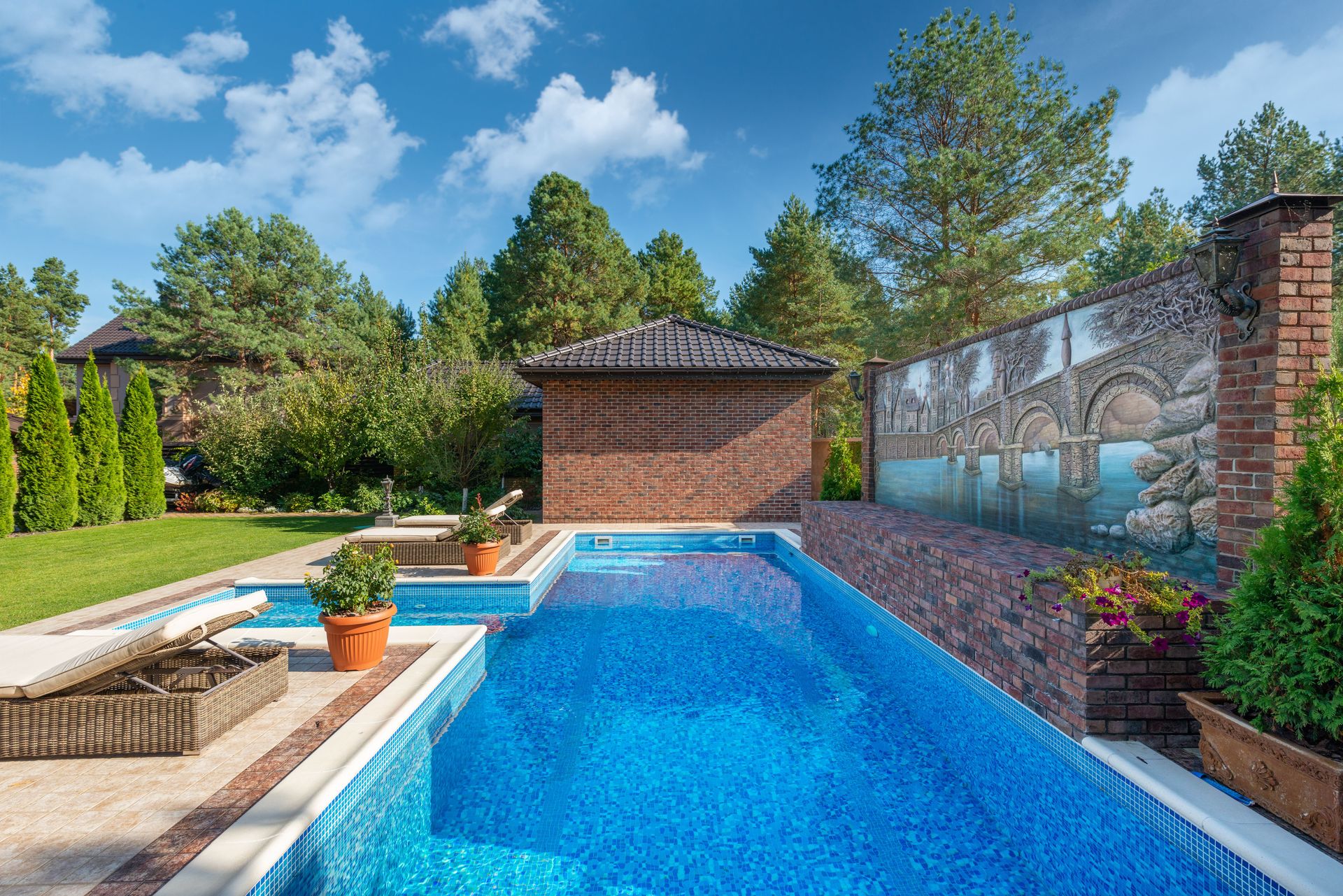 Blue backyard pool with brick patio, lounge chairs, and a stone wall under a sunny sky